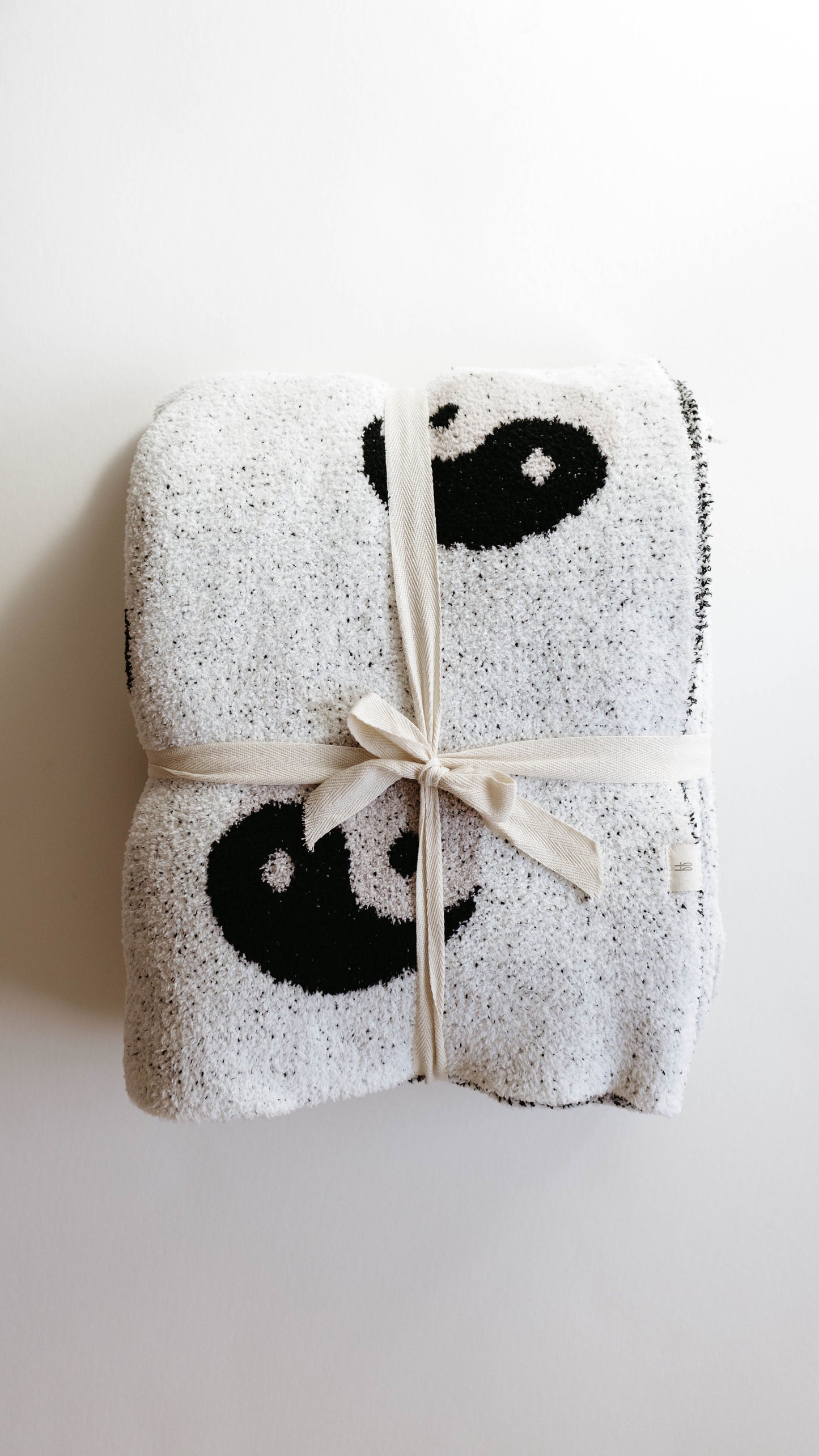 A neatly folded forever french baby Plush Blanket in gray, adorned with black and white yin-yang symbols, made from velvety-rich microfiber feather yarn and tied with a beige ribbon on a plain white background.