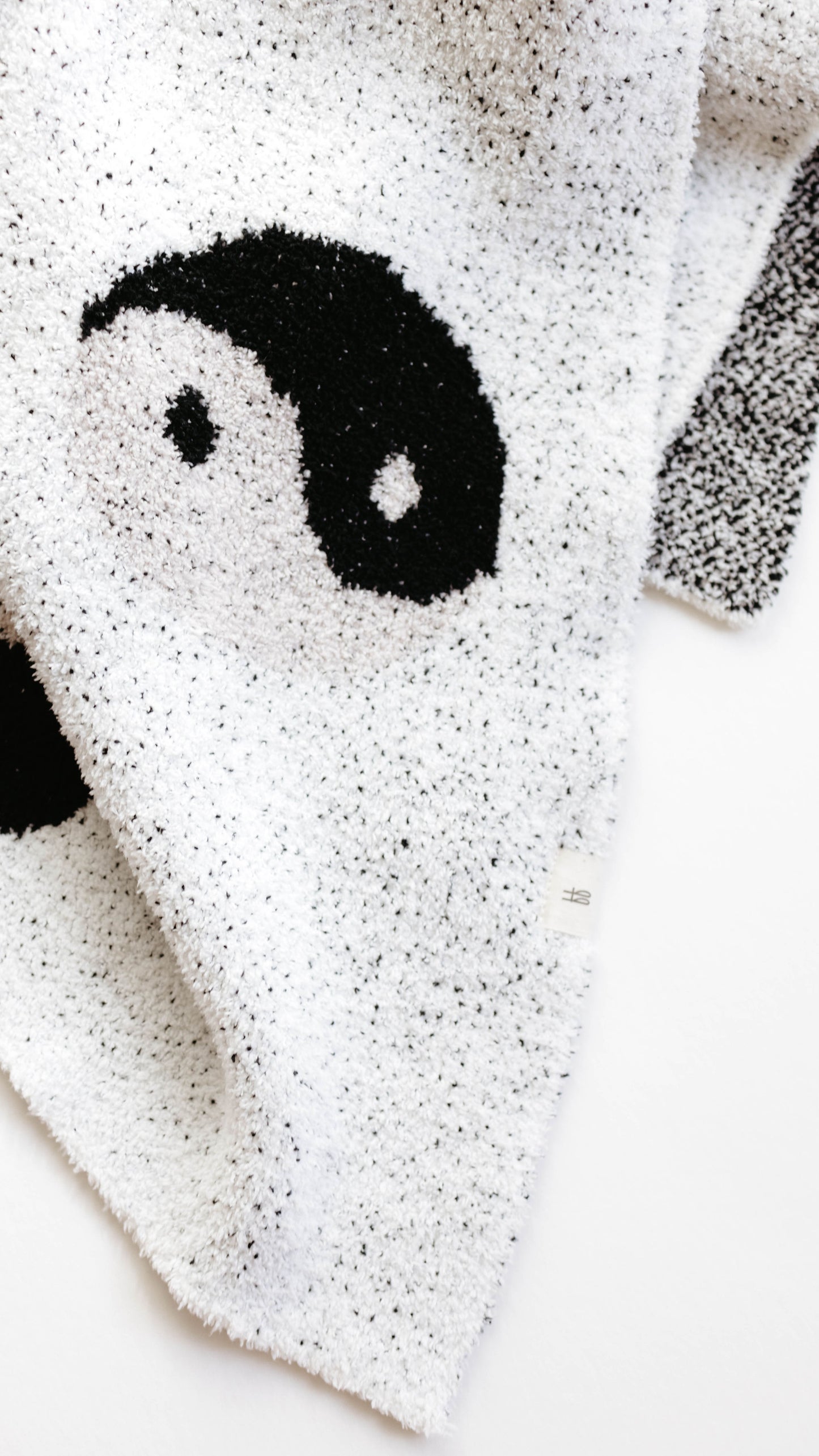 A close-up image of the forever french baby Plush Blanket | Black & White Yin Yang, showcasing its predominantly white textured fabric adorned with a black and white yin-yang symbol pattern. The velvety-rich texture of the blanket appears soft and is shown slightly folded over itself against a plain white background.