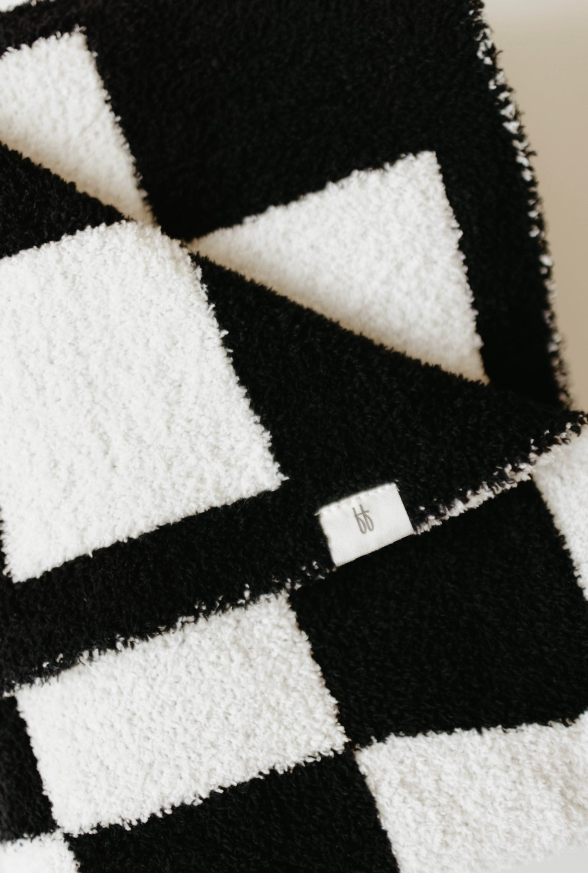 Close-up of a folded Plush Blanket | Black & White Checkerboard with a small tag displaying the forever french baby logo. The texture of this OEKO Standard 100 soft blanket appears incredibly soft and fuzzy.