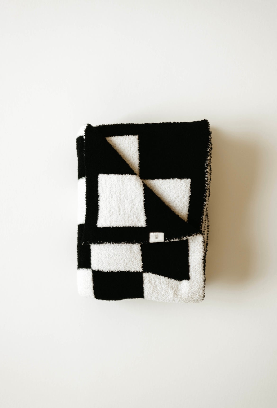 A folded Plush Blanket in a black and white checkerboard design with a soft, textured surface is displayed against a plain white background. The blanket, from forever french baby, features large squares in alternating colors, creating a bold geometric pattern and meets the OEKO Standard 100 for quality assurance.