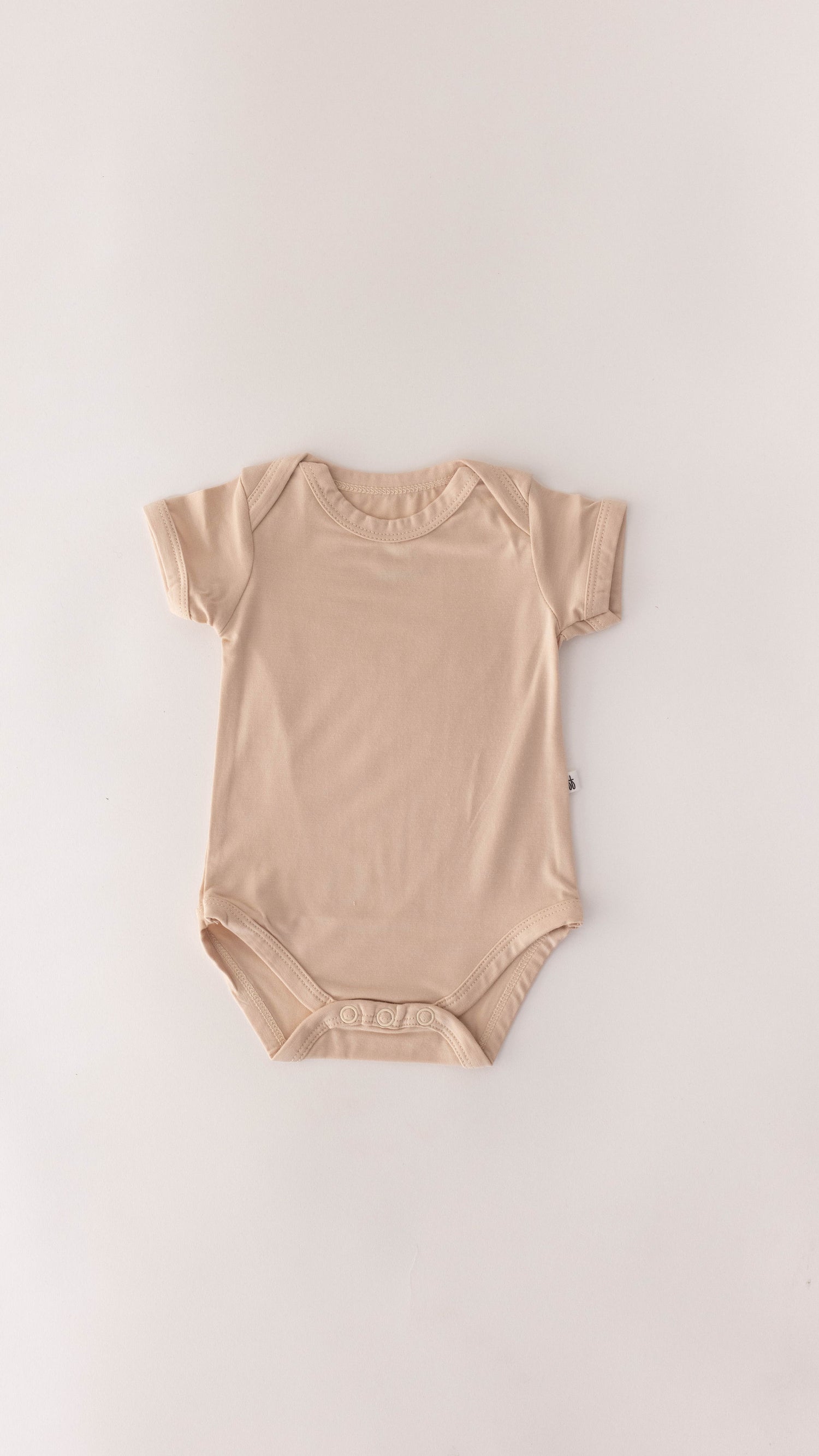 The "Cream | Bamboo Snapsuit" by forever french baby is a light beige, short-sleeved baby snap suit crafted from soft bamboo fabric. It features snap closures at the bottom for easy diaper changes and an envelope neckline for convenient dressing. Gender neutral and laid flat on a white background, it’s perfect for any baby.